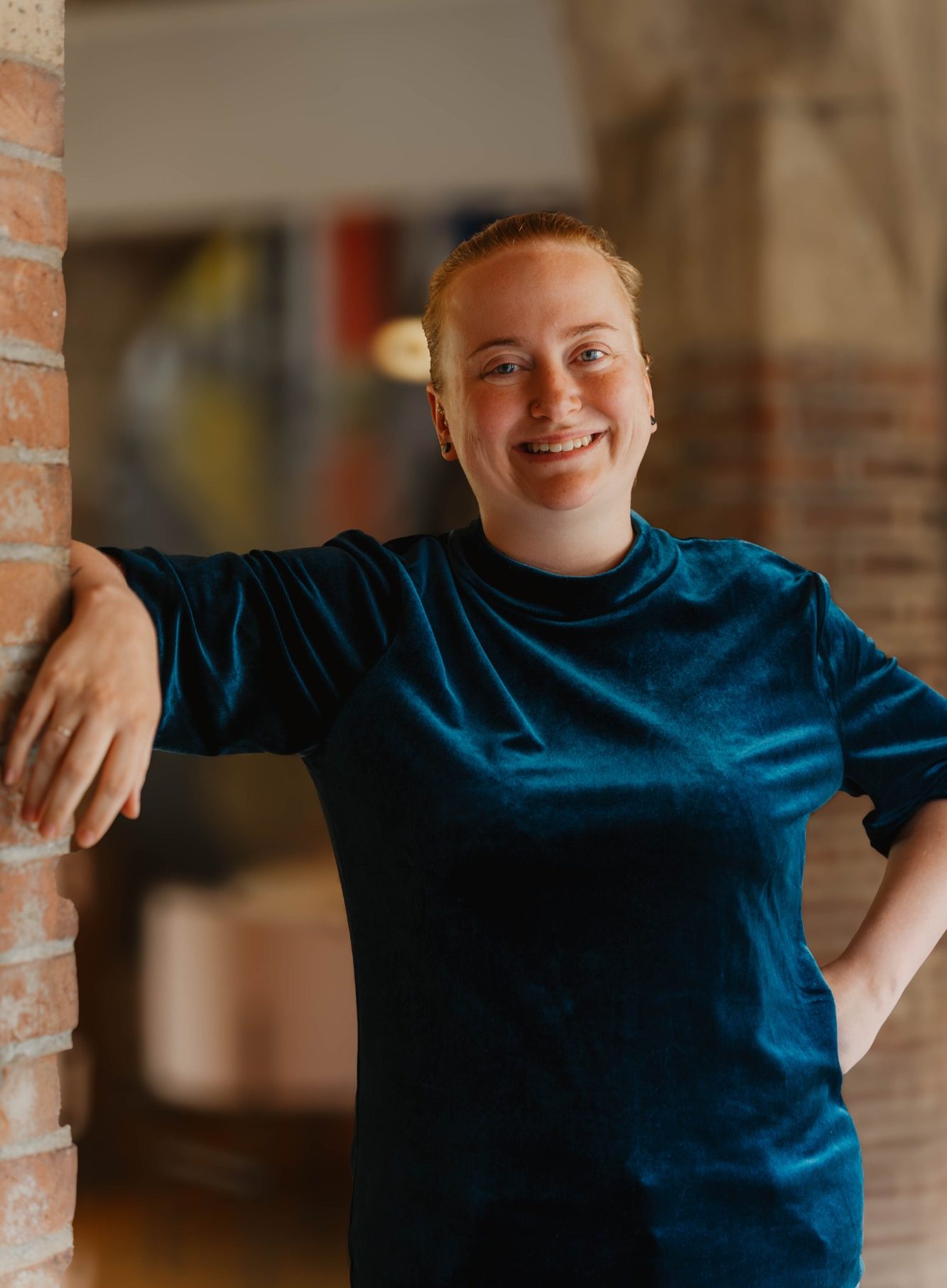 Taakmevrouw met een glimlach, gekleed in een groene outfit, staat tegen een muur.